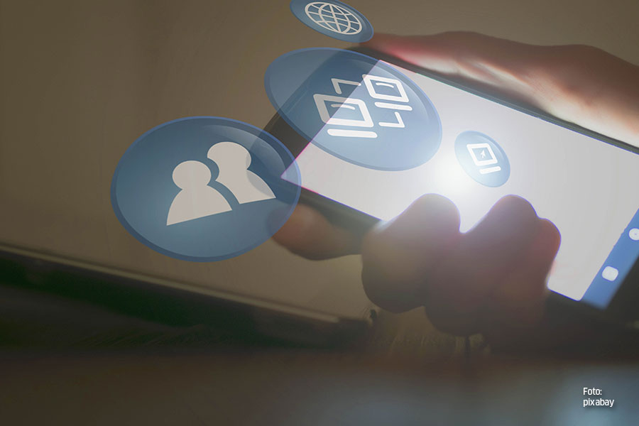 Eine leicht verschwommene Bildaufnahme. Eine Hand hält ein Smartphone. Grafisch verdeutlichen vier verschiedene Icons die Digitalisierung.