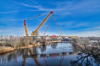 Ein Kran hebt die neue Brücke über die Uferkanten des Ruderkanals in der Saaleaue.