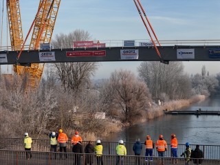 Nach dem gelungenen Aufsetzen der Brücke über die Uferkanten sind die Projektverantwortlichen zufrieden. Sie stehen mit dem Rücken zum Fotografen und blicken auf die neue Brücke.